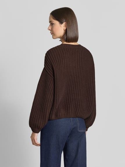 Frauenmodel trägt Relaxed Fit Strickpullover aus Baumwoll-Mix von Apricot, dunkelbraune Grobstrickstruktur, gerippte Abschlüsse, Ganzkörperansicht Rückansicht.