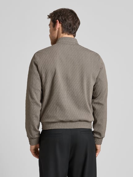 Männermodel trägt Jacke aus Schurwoll-Mix mit Zweiwege-Reißverschluss von Emporio Armani in Beige, strukturiertes Material, Rückansicht Ganzkörperansicht. Regular Fit, Stehkragen, Stretch-Anteil, Eingrifftaschen, bei Größe 50 Rückenlänge 63 cm, Schulterbreite 45 cm, Brustweite 53 cm, Ärmellänge 67 cm.