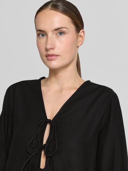 Frauenmodel trägt Blusenshirt aus Viskose-Mix mit Schnürung von Vila, schwarz, mit V-Ausschnitt, Regular-Fit, Nahaufnahme Oberkörper. Kontext: Damen Blusenshirt, Viskose-Mix mit Leinen-Anteil, Modell 'PRISILLA', Rückenlänge bei Größe 36: 56 cm, Ärmellänge: 61 cm.
