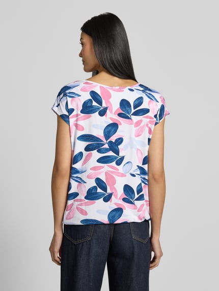 Vrouwenmodel draagt blouse met korte mouwen van ZABAIONE, mix van viscose en elastaan, los model, Model 'Minou', ruglengte maat S 56 cm, blauw en roze bladmotief, elastische band, plooien, ronde hals, met korte mouwen. Ganzkörperansicht Rückansicht.