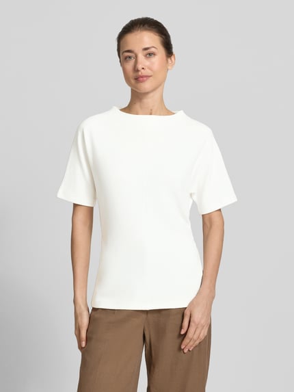 Kobieta prezentuje damski t-shirt z mieszanki wiskozy z dodatkiem streczu, prosty krój, okrągły dekolt, fakturowany wzór, model 'Kavora' od Someday, długość tyłu w rozmiarze 36: 62 cm, jasna kolorystyka, widok całej sylwetki z przodu.