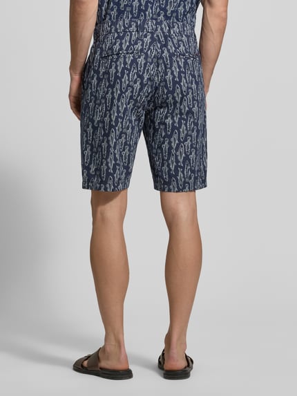 Męski model nosi Chino Shorts mit französischen Eingrifftaschen od Lerros, bawełniany miks z lnem, krój straight fit, elastyczny pas ze sznurkiem, kieszenie francuskie i tylne, szerokość w rozmiarze 32: 42 cm, długość nogawki od wewnątrz: 24 cm, granatowy wzór, tekstura gładka, całość z tyłu