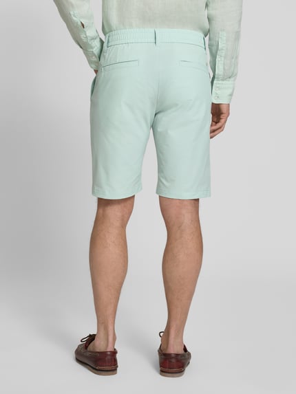 Männermodel trägt Tapered Fit Bermuda mit Kordelzug Modell 'CHINO' von BOSS Orange in Mint mit Allover-Muster, Ganzkörperansicht Rückansicht.