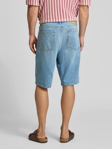Männermodel trägt Loose Fit Jeansshorts aus Lyocell-Baumwoll-Mix Modell 'BAGGY HEMP BLEND' von Armedangels in heller Denim-Optik, 5-Pocket-Design, Label Patch, Ganzkörperansicht Rückansicht.
