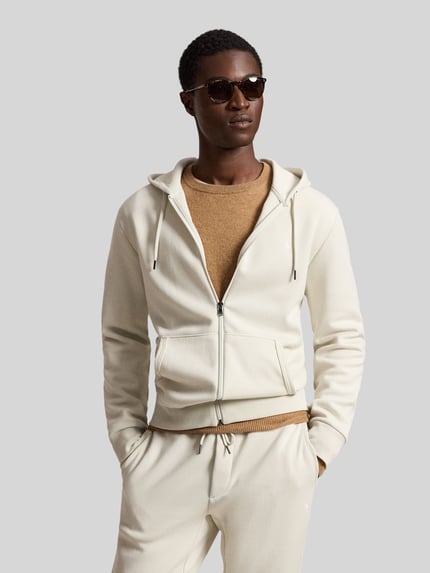 Männermodel trägt Regular Fit Sweatjacke aus Baumwoll-Mix von Polo Ralph Lauren in Creme mit Reißverschluss, beiger Pullover, Ganzkörperansicht von vorne.
