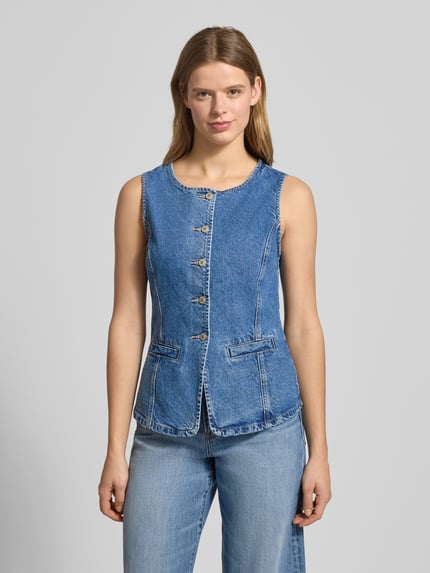 Frauenmodel trägt Jeansweste aus reiner Baumwolle Modell 'GUILINA' von ONLY in blauer Denim-Optik, Paspeltaschen, Rundhals, einreihige Knopfleiste, Ganzkörperansicht von vorne.