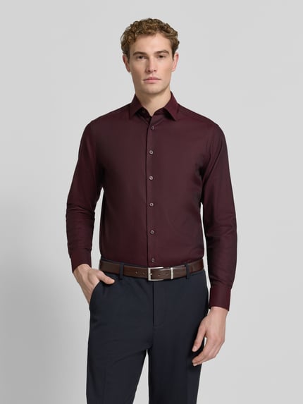 Männermodel trägt Regular Fit Businesshemd mit Kentkragen von OLYMP in dunklem Rot, feines Webstruktur, unifarben, Ganzkörperansicht von vorne.