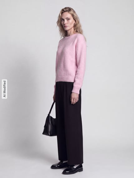 Kobieta modelka ma na sobie sweter Regular Fit Pullover mit Woll-Anteil Modell 'ALLY' od PIECES w jasnoróżowym kolorze, proste czarne spodnie, czarne buty, trzyma czarną torebkę, matowe tło, całkowity widok z przodu, KI-modifiziertes Bild.