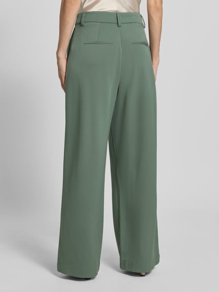 Frauenmodel trägt Wide-Leg-Pants mit Biesen Modell 'Henrika' von MSCH Copenhagen aus grünem Material-Mix mit Viskose-Anteil, Gesäßleistentaschen, ausgestellt geschnitten, Ganzkörperansicht Rückansicht.