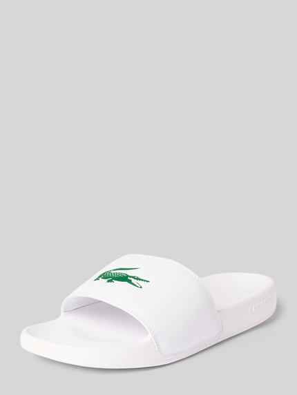 Produktfoto, Badeschuhe mit Logo Print Modell 'SERVE SLIDE' von Lacoste, biała jednolita optyka, zaokrąglony nosek, płaski obcas, strukturalna podeszwa, aplikacja z logo, wsuwane