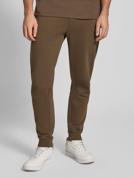 Męski model nosi Comfort Fit Sweatpants aus reiner Baumwolle Modell 'NAPIN' od Hugo Blue, brązowy, prosta tekstura, widok z przodu, zbliżenie na dolną część ciała.
