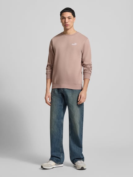 Męski model nosi Regular Fit Sweatshirt mit Logo-Stitching od PUMA PERFORMANCE, mieszanka bawełny, okrągły dekolt, elastyczne wykończenia, długość tyłu 69 cm, długość rękawów 69 cm, widok całej sylwetki z przodu.