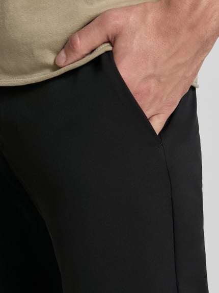 Männermodel trägt Tapered Fit Hose mit Gesäßtaschen von MCNEAL in Schwarz, glatte Textur, sichtbare Eingrifftaschen, Nahaufnahme Oberkörper. Bundweite bei Größe M: 45 cm, Innenbeinlänge bei Größe M: 80 cm, Knopf- und Reißverschluss.