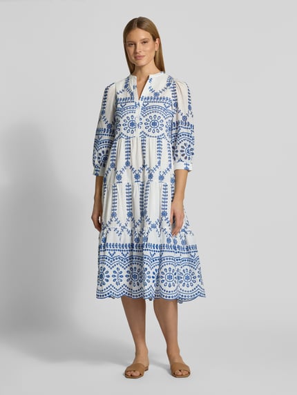 Vrouwenmodel draagt Tunikakleid mit Volantsaum und Lochstickerei van Apricot in wit met blauw, puur katoen, los model, serafinokraag, ajourwerk, korte knoopsluiting, volantzoom, midilengte, ruglengte maat S 110 cm, borstwijdte maat S 46 cm, mouwlengte maat S 52 cm, volledig zicht van voren.