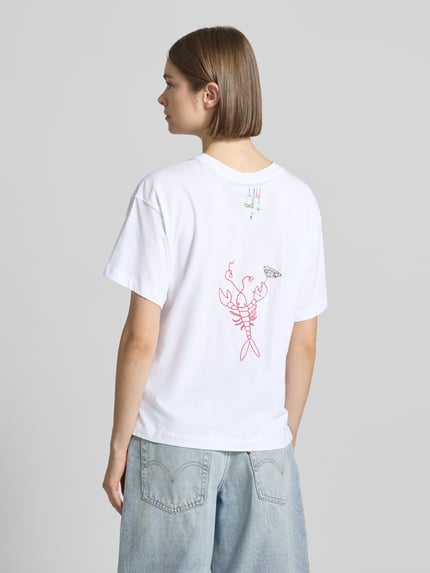 Modelka nosi Regular Fit T-Shirt aus reiner Baumwolle Modell 'EMMINA' von Only; biała, haftowana, krój regular fit, widok z tyłu