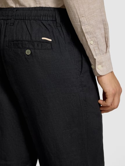 Mężczyzna nosi Leinenhose mit elastischem Bund Modell 'KARL LAWRENCE' von Jack & Jones, czarny, krój regular fit, czysta len, widoczny elastyczny pas; Szerokość w rozmiarze M: 40 cm, długość nogawki od wewnątrz: 75 cm; zbliżenie na tył spodni.