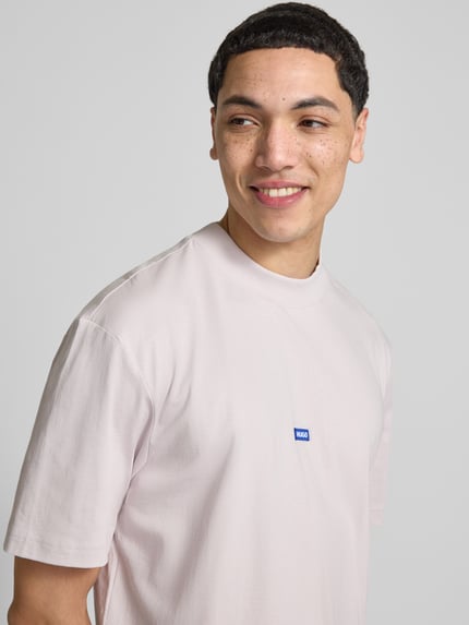 Mężczyzna nosi Regular Fit T-Shirt aus reiner Baumwolle Modell 'Niereos' von HUGO Blue, jednolity kolor, krótki rękaw, naszywka z logo, okrągły dekolt, materiał jersey z czystej bawełny, zbliżenie na górną część ciała.