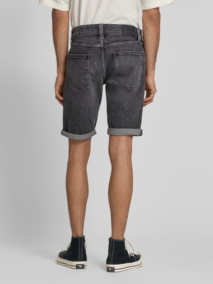 Männermodel trägt schwarze Regular Fit Jeansshorts aus Baumwoll-Mix von Tommy Jeans mit 5-Pocket-Design, Label-Patch, Logo-Stitching, Ganzkörperansicht Rückansicht.