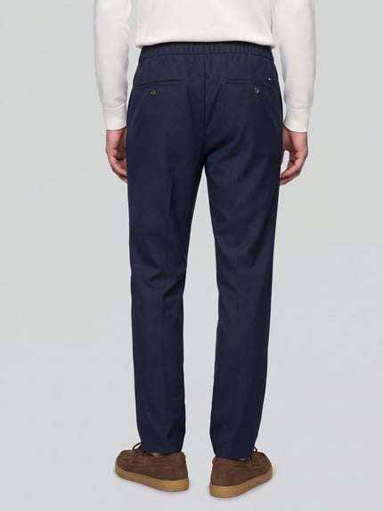 Männermodel trägt Low Waist Stoffhose mit Logo-Detail von Tommy Hilfiger, dunkelblau, Wollmix mit feinem Webstruktur, Ganzkörperansicht Rückansicht.