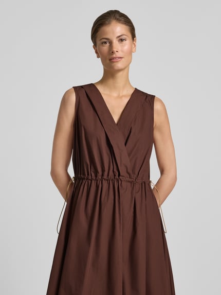 Frauenmodel trägt knielanges Cocktailkleid mit Kordelzug und Kordelstoppern von Rinascimento aus Reine Baumwolle, Taillierter Schnitt, V-Ausschnitt, in Braun mit feiner Textur, Nahaufnahme Oberkörper.