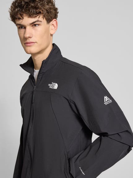 Männermodel trägt Regular Fit Jacke mit Stehkragen Modell 'Mountain' von The North Face in Schwarz mit Logo-Print, Reißverschluss und Eingrifftaschen, Elastischer-Material-Mix, Nahaufnahme Oberkörper.