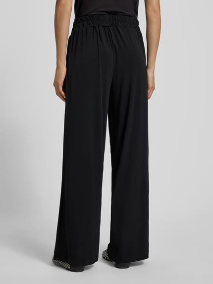 Frauenmodel trägt Stoffhose in verkürzter Passform Modell 'LIMA' von ICHI, schwarzer Material-Mix mit Stretch-Anteil, lockerer Schnitt, elastischer Bund, Ganzkörperansicht Rückansicht.