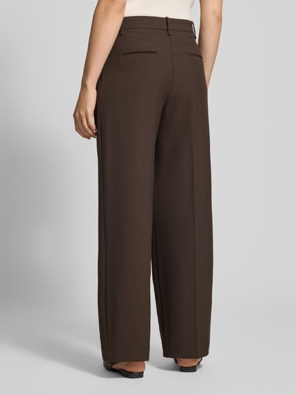 Frauenmodel trägt Bundfaltenhose aus Viskose-Mix Modell 'LEO' von MANGO, braun, Relaxed Fit, Detailansicht Gesäßtaschen, Ganzkörperansicht Rückansicht.