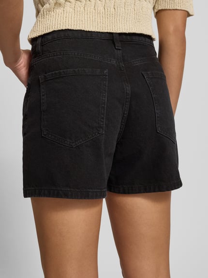 Frauenmodel trägt Jeansshorts im 5-Pocket-Design Modell 'ZOEY' von Mango aus Reine Baumwolle, Straight, schwarze Waschung, Ganzkörperansicht Rückansicht.