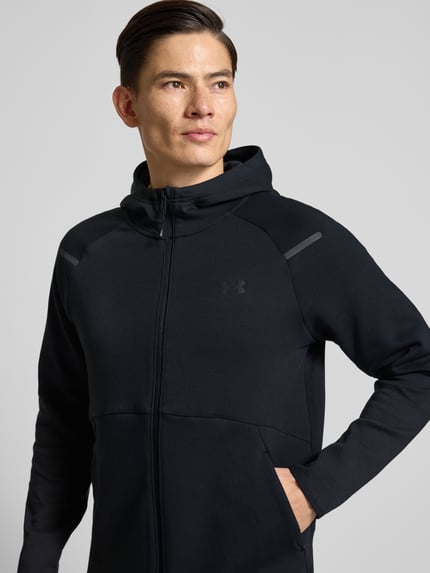 Männermodel trägt schwarze Trainingsjacke mit Zweiwege-Reißverschluss Modell 'Unstoppable' von Under Armour, Material-Mix, Kapuze, Regular-Fit, Nahaufnahme Oberkörper.