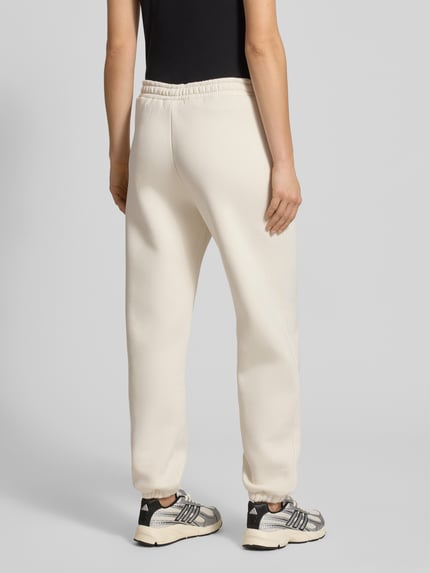 Vrouwenmodel draagt Basic Sweatpant met boordjes aan de zoom en zijzakken van review, katoenmix, los model, binnenbeenlengte maat S 74 cm, geborduurd logo, labelprint, kleur licht, textuur glad, geheel uitzicht achterkant.