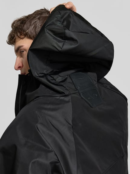 Männermodel trägt Regenjacke mit Pattentaschen von VETEMENTS, schwarz, Kapuze mit Tunnelzug, lockere Passform, Nahaufnahme Oberkörper