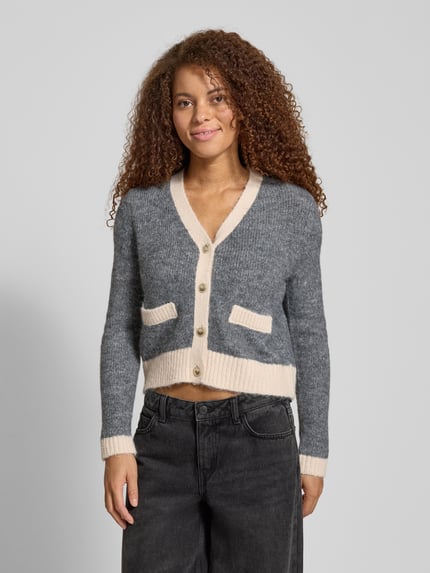 Vrouwenmodel draagt Shaped Fit Strickjacke met wol-aandeel model 'MAGGIE LIFE' van Only, meerkleurig, V-hals, ribboorden, label stitching, zakkendetail. Vooraanzicht bovenlichaam.