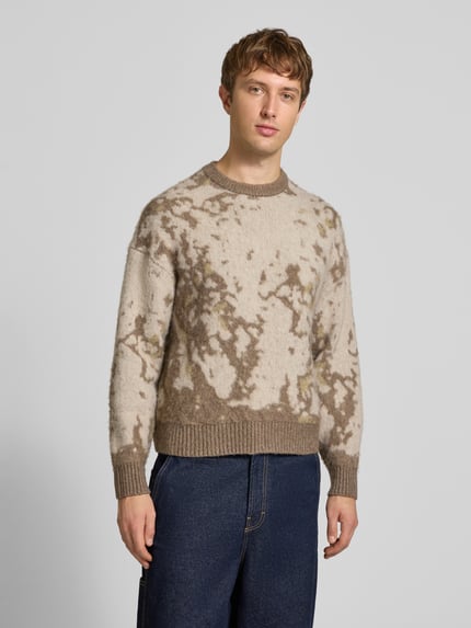 Männermodel trägt Pullover mit gerippten Abschlüssen von ONLY, mehrfarbig, abstraktes Allover-Muster, Strickoptik, Ganzkörperansicht von vorne.