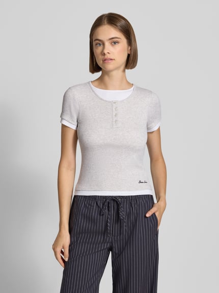 Modelka prezentuje Slim Fit T-Shirt mit Logo-Stitching od GUESS, fakturowany wzór, okrągły dekolt, krótki rękaw, długość tyłu w rozmiarze S: 50 cm, widok całej sylwetki z przodu.