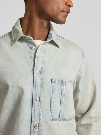 Männermodel trägt Regular Fit Jeanshemd mit Brusttasche Modell 'DAMON' von Samsøe Samsøe aus reiner Baumwolle, Nahaufnahme Oberkörper.