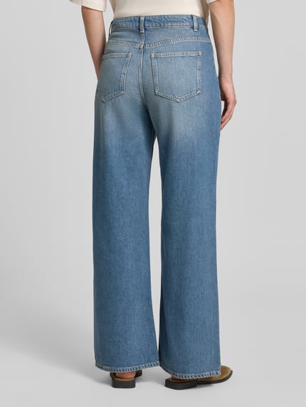 Frauenmodel trägt Wide Fit Jeans mit Lyocell-Anteil von Jake*s Casual in klassischem Blau, breite Beinform, Gesäßtaschen, Ganzkörperansicht Rückansicht. Baumwoll-Mix, aufgesetzte Taschen, Knopf- und Reißverschluss, Bundweite 38 cm, Innenbeinlänge 75 cm bei Größe 36.