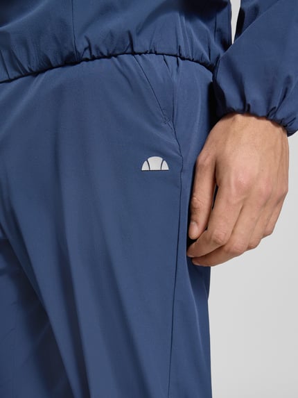 Männermodel trägt Trackpants mit elastischem Bund Modell 'EVARO' von Ellesse, tiefblau, glatte Textur, Regular Fit, Nahaufnahme Oberkörper.