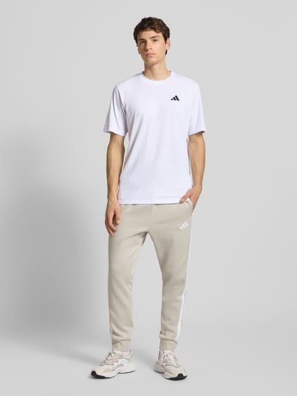 Männermodel trägt T-Shirt mit Label-Print von adidas Training in Weiß, Regular Fit, Baumwoll-Mix, Rundhalsausschnitt, Ganzkörperansicht von vorne.