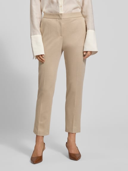 Kobiece model prezentuje Regular Fit schmale Hose aus Viskose-Mix Model 'Tapria-Crop4' od BOSS, beżowy kolor, tekstura gładka, długość do kostki, całkowity wzór, ozdobna kieszeń, zapięcie na guzik, schiebehaken i ukryty zamek, boczne kieszenie, rozcięcie na dole nogawek, widok całej sylwetki z przodu.
