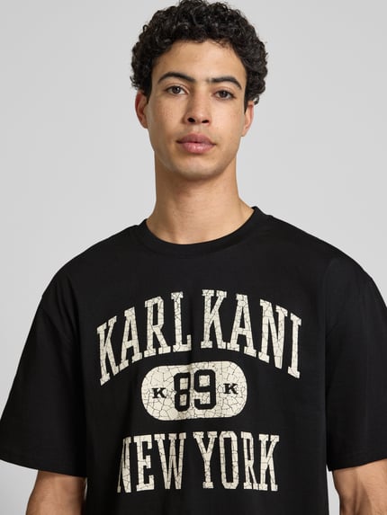 Männermodel trägt Oversized Fit Herren T-Shirt von KARL KANI aus Reine Baumwolle mit Logo-Print Modell 'Heritage', Rundhalsausschnitt, Nahaufnahme Oberkörper.