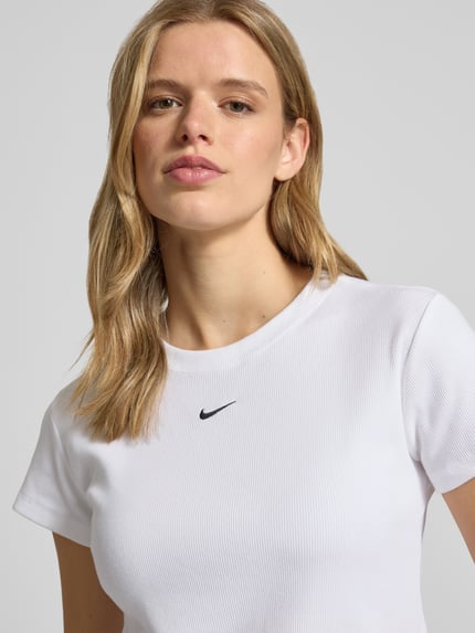 Frauenmodel trägt Cropped T-Shirt in Ripp-Optik mit Logo von Nike aus Baumwoll-Elasthan-Mix, Rundhalsausschnitt, Nahaufnahme Oberkörper.