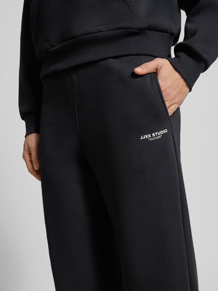 Frauenmodel trägt High Waist Sweatpants mit elastischem Bund und Logo von JJXX aus schwarzem Baumwoll-Mix, weites Bein, Nahaufnahme Oberkörper.