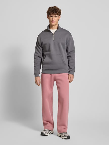 Mannenmodel draagt Loose Fit Sweatpants mit Seitentaschen van REVIEW in roze, katoenmix, met labelprint, elastische tailleband, zijzakken en achterzak; volledige lichaamsaanzicht van voren.