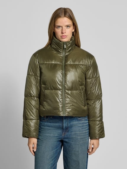 Frauenmodel trägt Puffer Jacket mit glänzender Optik von PIECES in Olivgrün, unifarben, cropped, sichtbare Teilungsnähte, Reißverschluss, elastische Abschlüsse, Ganzkörperansicht von vorne.