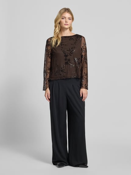 Frauenmodel trägt Kurz Langarmbluse mit Paillettenapplikation von PIECES aus schwarzem Chiffon mit floraler Spitze, Ganzkörperansicht von vorne.