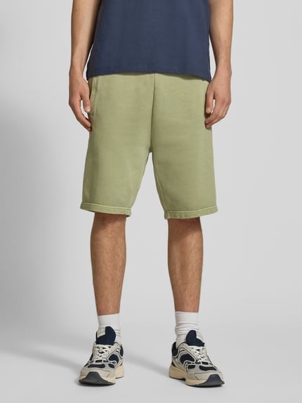 Männermodel trägt Sweatshorts mit Eingrifftaschen Modell 'Nelson' von Carhartt Work In Progress in Grün, Reine Baumwolle, Relaxed-Fit, Ganzkörperansicht von vorne.