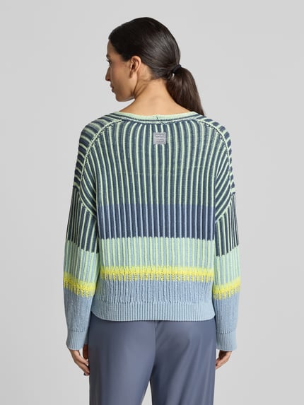 Frauenmodel trägt Oversized Strickpullover mit V-Ausschnitt von Marc Cain, gestreiftes Design in Blau, Gelb, Baumwoll-Mix, Ganzkörperansicht Rückansicht.