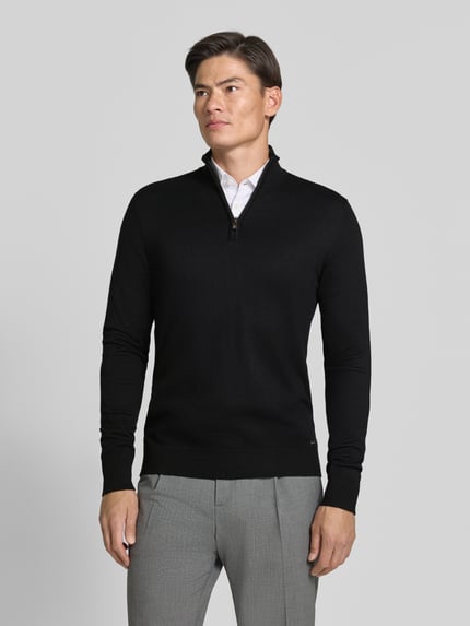 Männermodel trägt Troyer mit Label-Applikation von MARKUP in Schwarz, gerader Schnitt, gerippte Abschlüsse, Ganzkörperansicht von vorne.