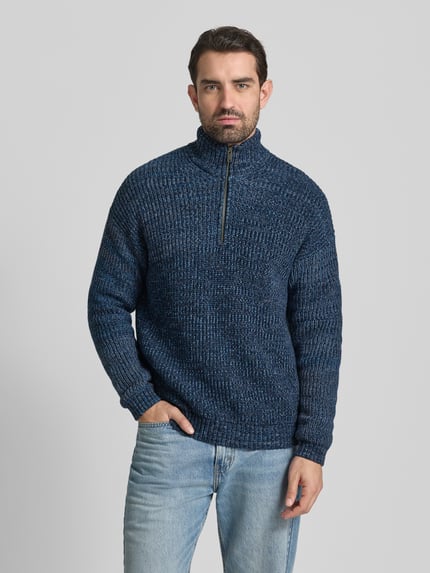 Männermodel draagt Relaxed Fit Troyer aus Baumwoll-Woll-Mix Modell 'MICHAAEL MOULINE' van Armedangels in blauwe melange, grofgebreid, met korte rits, opgestikte label patch, geribde boorden en lange mouwen; Ganzkörperansicht von vorne.