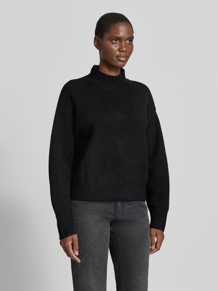 Frauenmodel trägt Turtleneck-Pullover mit Woll-Anteil und Rundhalsausschnitt von Neo Noir in Schwarz, gerader Schnitt, gerippte Abschlüsse, Ganzkörperansicht von vorne.